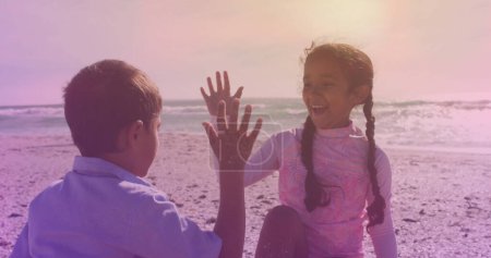 Spots of light against hispanic brother and sister high fiving each other at the beach. national siblings day awareness concept