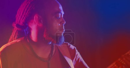 Photo for Image of red and blue light blurs over african american man with dreadlocks playing bass guitar. Live music, creativity, performance and entertainment concept digitally generated image. - Royalty Free Image
