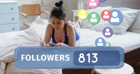 Close up of a Caucasian woman lying in bed while texting on her phone. Bellow her in the foreground is a digital image of a followers count bar with icons flying upwards