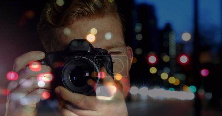 Kaukasische männliche Fotografen klicken Bilder mit Digitalkamera gegen den nächtlichen Stadtverkehr. Weltfototag-Konzept