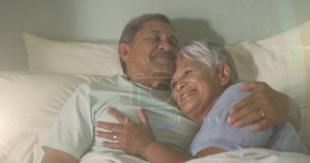 Photo for Image of glowing lights over happy senior couple lying in bed in background. retirement and senior life concept digitally generated image. - Royalty Free Image