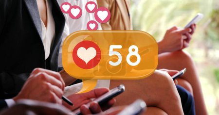Foto de Imagen digital de un icono del corazón y números crecientes dentro de una caja de chat amarilla. Hay gente con atuendos corporativos sentados en fila mientras revisa sus teléfonos 4k - Imagen libre de derechos
