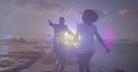 Téléchargez les photos : Point lumineux contre la vue arrière du couple afro-américain courant sur les rochers près de la mer. Concept d'amour et de relation - en image libre de droit