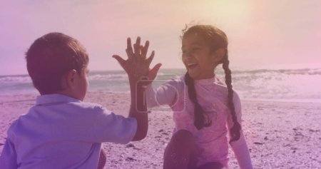 Photo for Spots of light against hispanic brother and sister high fiving each other at the beach. national siblings day awareness concept - Royalty Free Image