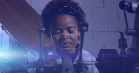 Téléchargez les photos : Image d'une lumière brillante sur une femme afro-américaine travaillant dans un atelier. journée du travail, travail, travailleurs, tradition et concept de célébration image générée numériquement. - en image libre de droit