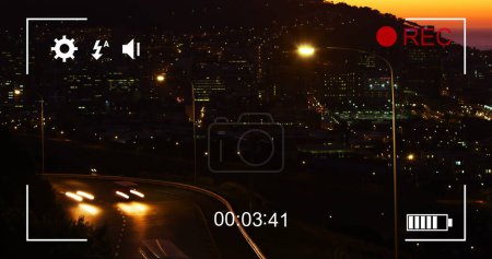 Image of night traffic in fast motion and cityscape, seen on a screen of a digital camera in record mode with icons and timer 