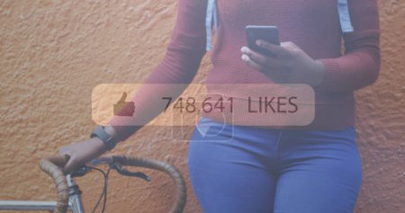 Photo for Image of social media notification over african american woman with bike using smartphone. global communication technology and social network concept digitally generated image. - Royalty Free Image