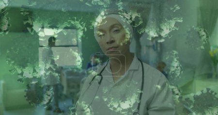 Foto de Imagen de una doctora mirando la cámara en el hospital con células coronavirus flotando en primer plano. Covid 19 pandemia salud ciencia medicina concepto digital compuesto - Imagen libre de derechos