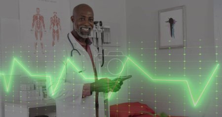 Image of cardiograph over happy african american male doctor with tablet. Medicine, health and digital interface concept, digitally generated image.