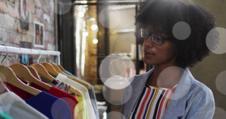 Foto de Imagen de manchas de luz sobre mujer afroamericana en tienda de ropa. concepto de redes, negocios y conexiones globales imagen generada digitalmente. - Imagen libre de derechos