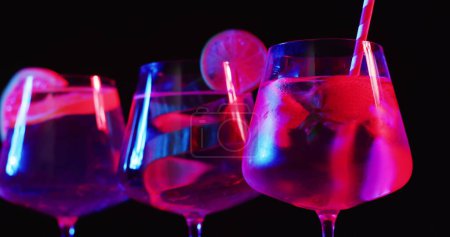 Photo for Glasses filled with vibrant drinks glow under neon lights. The scene captures a festive atmosphere, in a bar or at a party. - Royalty Free Image