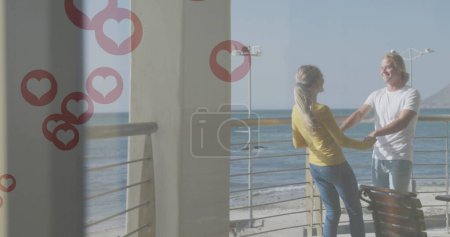 Téléchargez les photos : Plusieurs icônes de coeur rouge flottant contre couple caucasien dansant dans le balcon. réseautage social et concept de technologie - en image libre de droit