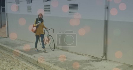 Image of light spots over biracial woman walking with bike. walk day and celebration concept digitally generated image.