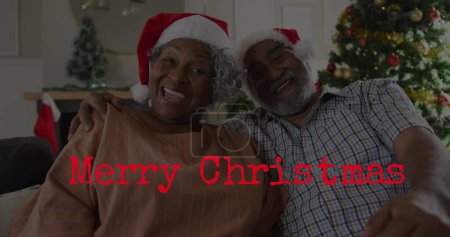 Photo for Image of merry christmas text over senior african american couple wearing santa hats. Christmas, tradition and celebration concept digitally generated image. - Royalty Free Image
