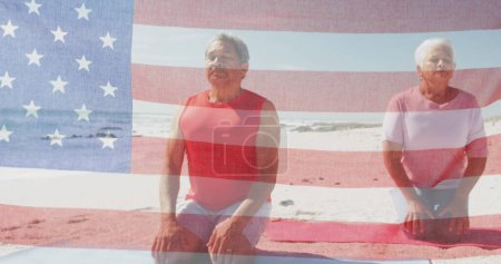 Foto de Imagen de bandera de estados unidos de América sobre pareja biracial mayor meditando en la playa. Patriotismo americano, diversidad y tradición concepto de imagen generada digitalmente. - Imagen libre de derechos