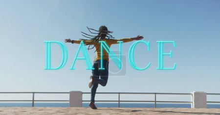 Foto de Banner de texto de baile de neón contra mujer afroamericana bailando en el paseo marítimo. concepto de baile y hobby - Imagen libre de derechos