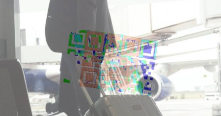 Foto de Imagen de un colorido código QR en un bucle sobre un hombre biracial llevando su maleta, caminando por un aeropuerto. Imagen compuesta digital - Imagen libre de derechos