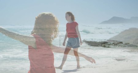 Photo for Full view of a Caucasian woman walking barefoot on the shore with a transparent image of her dancing in the foreground - Royalty Free Image