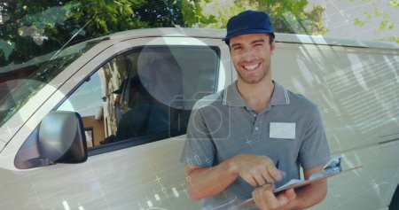 Photo for Front view of a deliveryman beside a van writing on a clipboard smiles and signals a thumbs up. Digital image of graphs and statistics are seen running in the foreground - Royalty Free Image