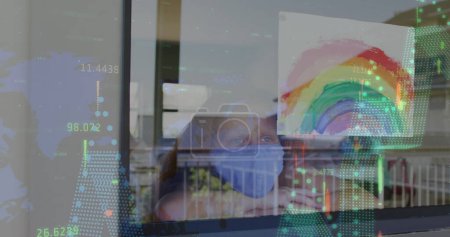 Image of statistics and girl in face mask by window with rainbow drawing. Healthcare and protection during coronavirus covid 19 pandemic, digitally generated image.