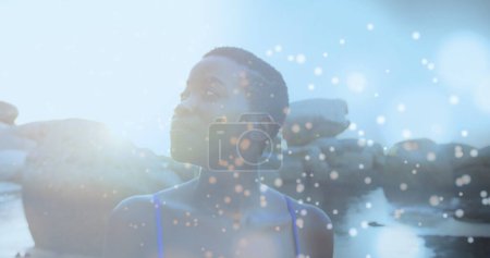 Foto de Manchas azules brillantes de luz contra la mujer afroamericana caminando sobre las rocas cerca del mar. Concepto de viajes y vacaciones - Imagen libre de derechos