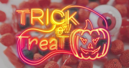 Téléchargez les photos : Neon trick or treat text banner with pumpkin icon against scary eye toy and halloween bondies. fête d'Halloween et concept de célébration - en image libre de droit