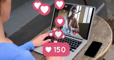 Photo for Person engages in a video call, floating hearts indicating affection. The scene suggests a virtual date or a loving conversation online. - Royalty Free Image