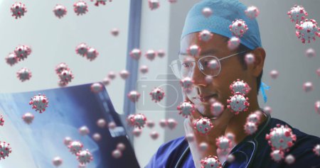Foto de Imagen de un médico masculino examinando una imagen de rayos X en el hospital con células del coronavirus flotando en primer plano. Covid 19 pandemia salud ciencia medicina concepto digital compuesto - Imagen libre de derechos