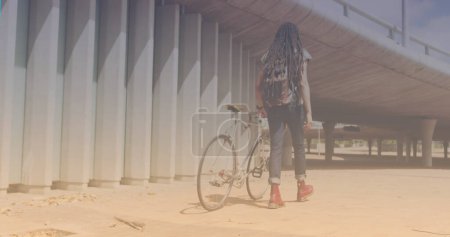 Téléchargez les photos : Spots of light against rear view of african american man with bicycle walking. pedal day awareness concept - en image libre de droit