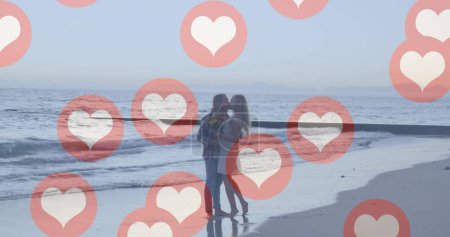 Téléchargez les photos : Plusieurs icônes de coeur rouge flottant contre couple caucasien embrassant sur la plage. réseautage social et concept de technologie - en image libre de droit