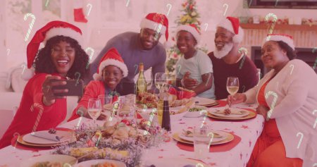 Téléchargez les photos : Image de cannes de bonbons tombant sur une famille souriante avec des chapeaux de Père Noël prenant selfie. Noël, hiver, tradition et concept de célébration image générée numériquement. - en image libre de droit