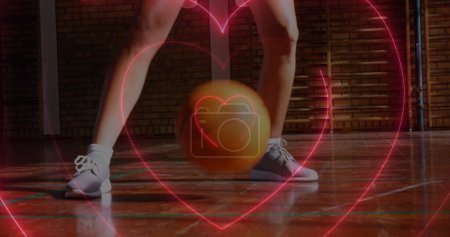 Téléchargez les photos : Image de cœurs de néon sur caucasienne joueuse de basket-ball rebondissant balle. Sport, fitness, mode de vie actif et fonctions de vie concept de surveillance image générée numériquement. - en image libre de droit