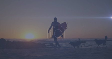 Foto de Punto de luz moviéndose contra la vista trasera de un hombre con tabla de surf caminando en la playa. Concepto de viajes y vacaciones - Imagen libre de derechos