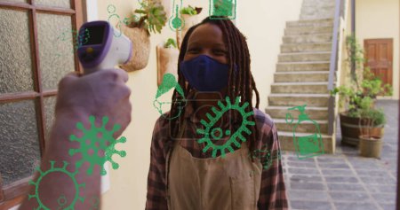 Bild von Virus-Ikonen über einer afrikanisch-amerikanischen Frau mit Gesichtsmaske, die Temperatur nimmt. Hobby während covid 19 Pandemiekonzept digital generiertes Bild.