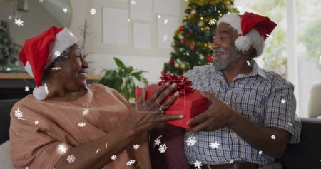 Bild von Schnee, der über ein älteres afrikanisch-amerikanisches Paar mit Weihnachtsmützen fällt. Weihnachten, Tradition und Festkonzept digital generiertes Image.