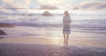 Rückansicht einer Frau, die bei Sonnenuntergang barfuß am Strand spaziert