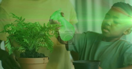 Photo for Image of lights over happy african american boy watering houseplants. childhood, independence, spending time at home concept digitally generated image. - Royalty Free Image