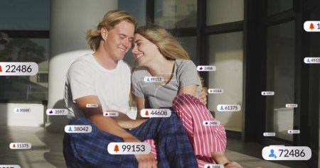 Image of social media notifications over smiling couple relaxing indoors in the sun. social media and global communication interface technology concept digitally generated image.