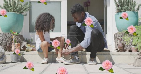 Image of roses over african american father tying shoes of his daughter. family life, love and care concept digitally generated image.