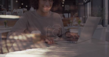 Image of smiling woman using laptop in cafe over sped up commuters walking in city. business and communication technology concept digitally generated image.