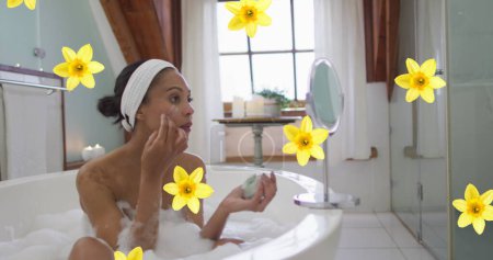 Téléchargez les photos : Image de fleurs jaunes sur femme biraciale relaxant dans le bain hydratant visage à la maison. concept de relaxation, santé et bien-être image générée numériquement. - en image libre de droit