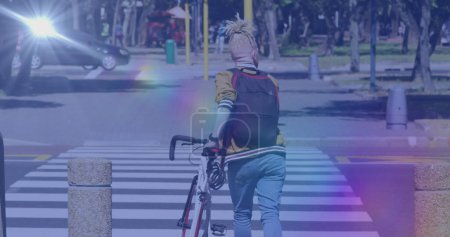 Foto de Imagen de manchas de luz sobre el hombre afroamericano albino caminando con bicicleta. bicicleta nacional para el día de trabajo y concepto de celebración de imagen generada digitalmente. - Imagen libre de derechos