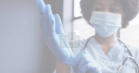 Foto de Imagen de 19 células covid con una doctora usando máscara poniéndose guantes. salud y protección durante coronavirus covid 19 pandemia, imagen generada digitalmente. - Imagen libre de derechos