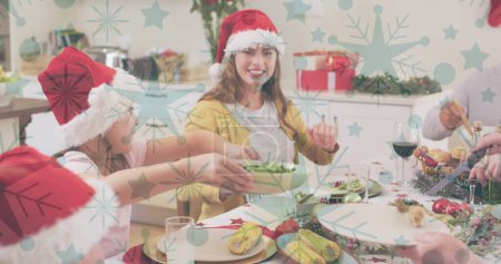 Image of snow falling over smiling caucasian family with santa hats having dinner. christmas, winter, tradition and celebration concept digitally generated image.