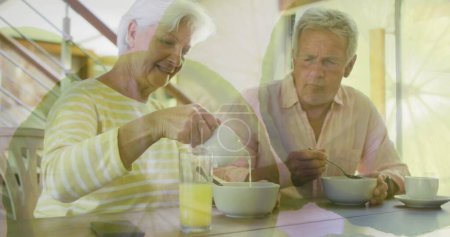 Photo for Image of orange slices over happy caucasian senior couple having breakfast at home. retirement lifestyle, companionship and wellbeing concept digitally generated image. - Royalty Free Image