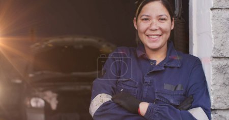 Bild von leuchtendem Licht über einer kaukasischen Automechanikerin in der Werkstatt. Arbeitstag, Arbeit, Arbeiter, Tradition und Festkonzept digital generiertes Image.