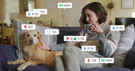 Photo for Image of social media icons and numbers over caucasian woman with pet dog at home. Global social media, data processing and digital interface concept digitally generated image. - Royalty Free Image