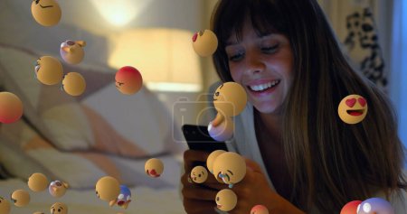 Photo for Image of emoji icons flying from right to left with a close up of a young Caucasian woman smiling and using a smartphone in the background 4k - Royalty Free Image