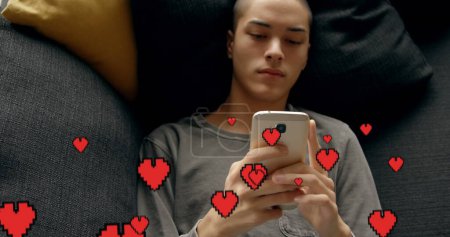 Foto de Compuesto digital de un hombre calvo caucásico acostado en la cama mensajes de texto y corazones digitales volando en primer plano. - Imagen libre de derechos