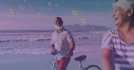 Téléchargez les photos : Icônes d'étoile d'or contre couple de personnes âgées afro-américaines avec vélo marchant ensemble à la plage. concept de sensibilisation à la journée pédale - en image libre de droit